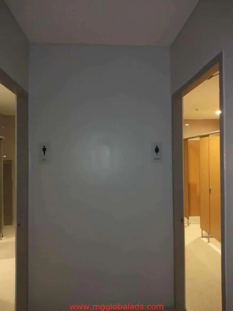 Restroom doors with metallic gender signage and beige stalls in a hallway, Makati location, by M&G Global Ads.