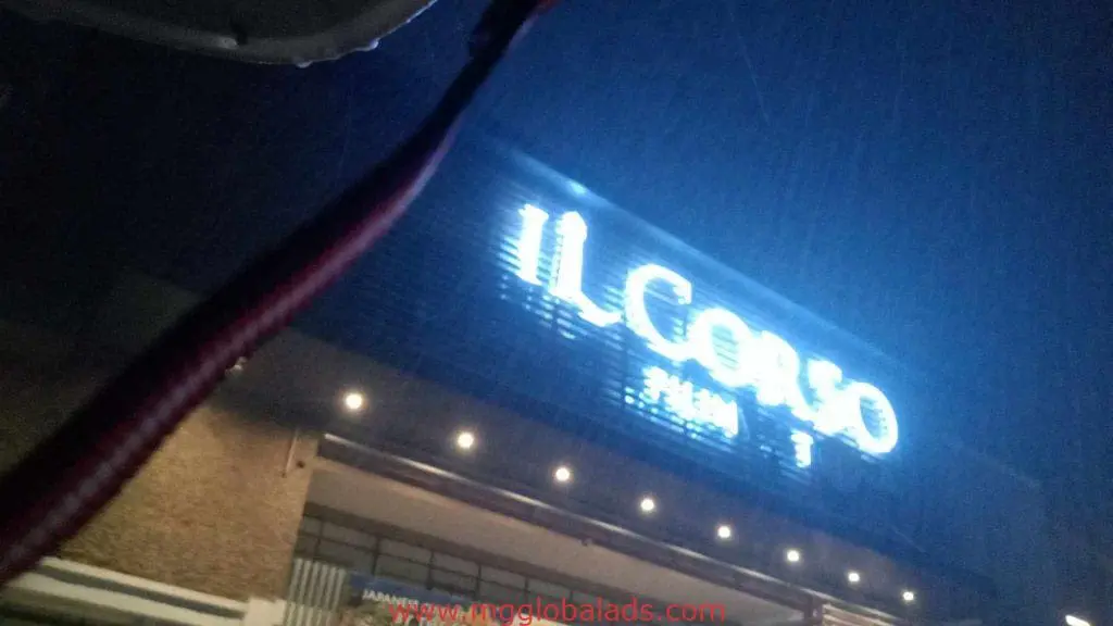 Nighttime shot of IL CORSO metallic signage in BGC, rain-blurred lights, foreground red and white strap, by M&G Global Ads.