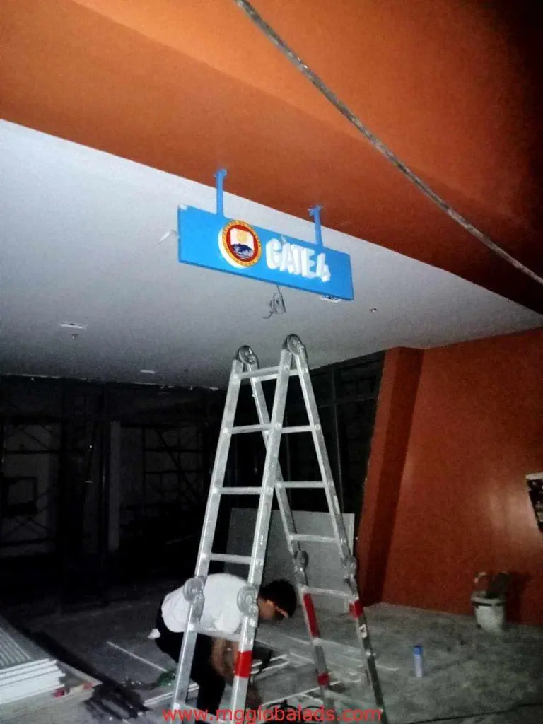 Indoor ceiling directional signage installation, GATE 4, in Makati by M&G Global Ads. Tools and materials visible on site.