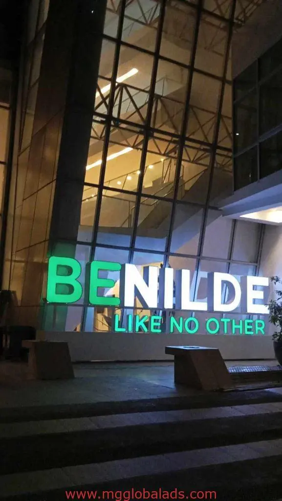 Illuminated building signage for Benilde outside modern glass building at night in Mandaluyong by M&G Global Ads.