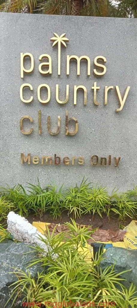 Building signage for Palms Country Club in gold letters on stone sign, greenery around, Makati. By M&G Global Ads.