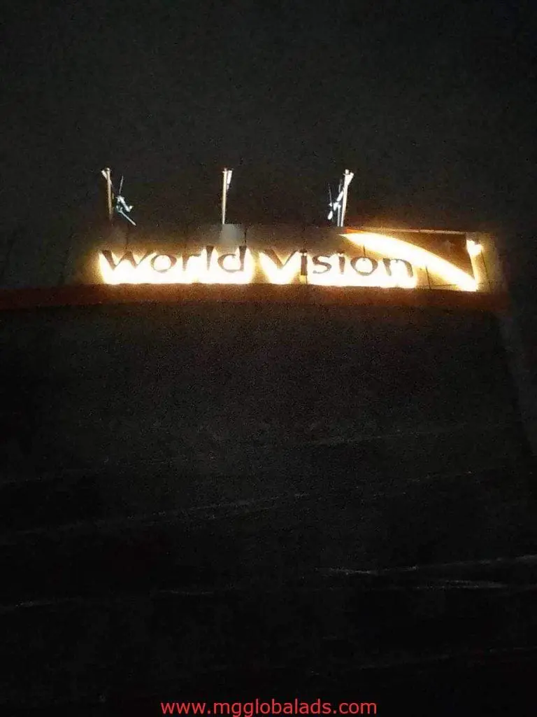 World Vision acrylic building signage glowing at night in Quezon City with flagpoles on top by M&G Global Ads.