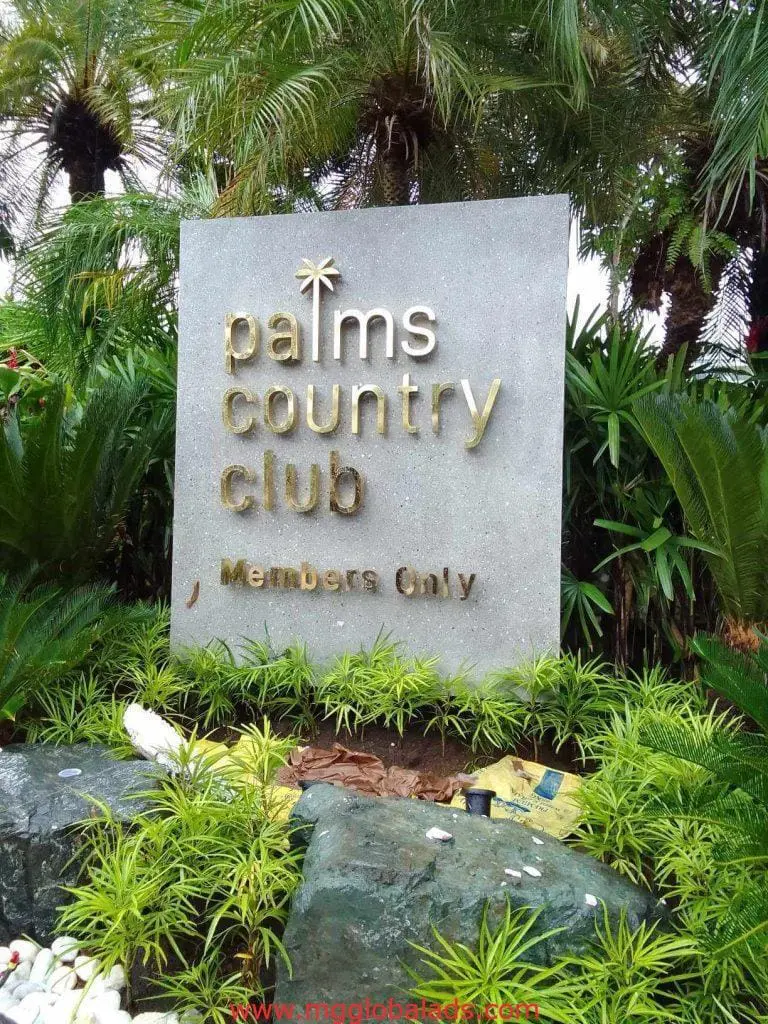 Stone outdoor signage for Palms Country Club in Makati with gold and white lettering, lush plants; by M&G Global Ads.