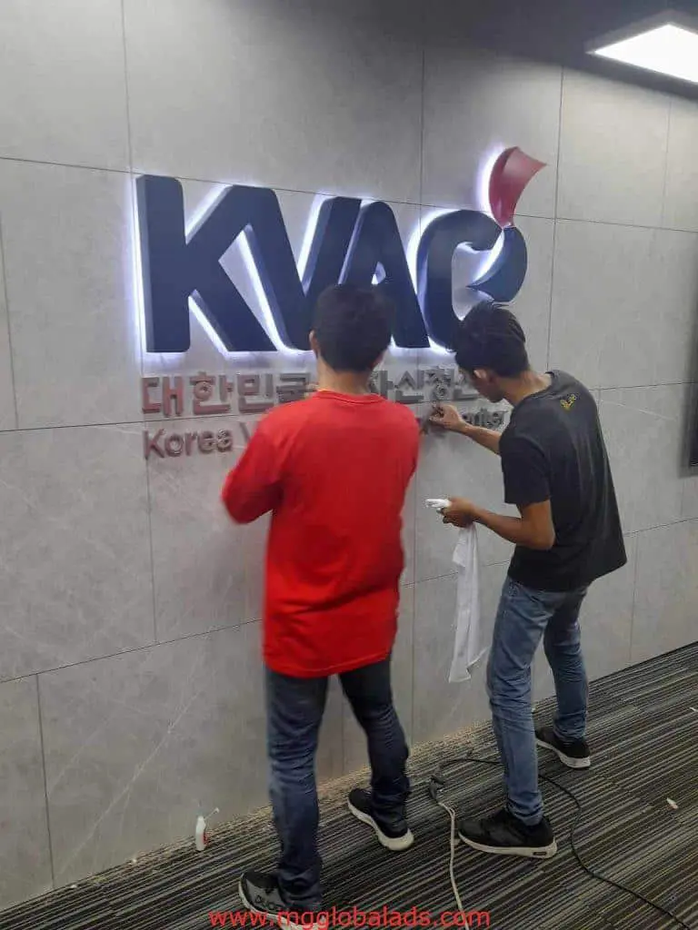 Acrylic indoor signage for KVAC with Korean text, being installed in a modern Quezon City office by M&G Global Ads.