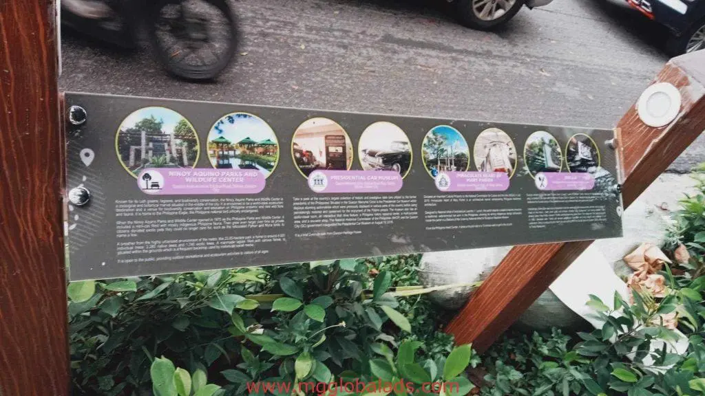 Informational outdoor signage on wooden posts with plants in Makati, street behind, by M&G Global Ads.
