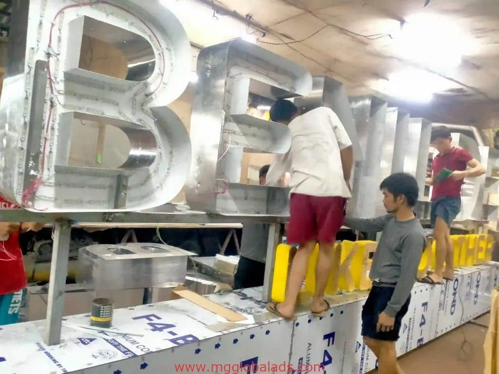 Workers assembling illuminated building signage for a client in Quezon City workshop, tools scattered, by M&G Global Ads.