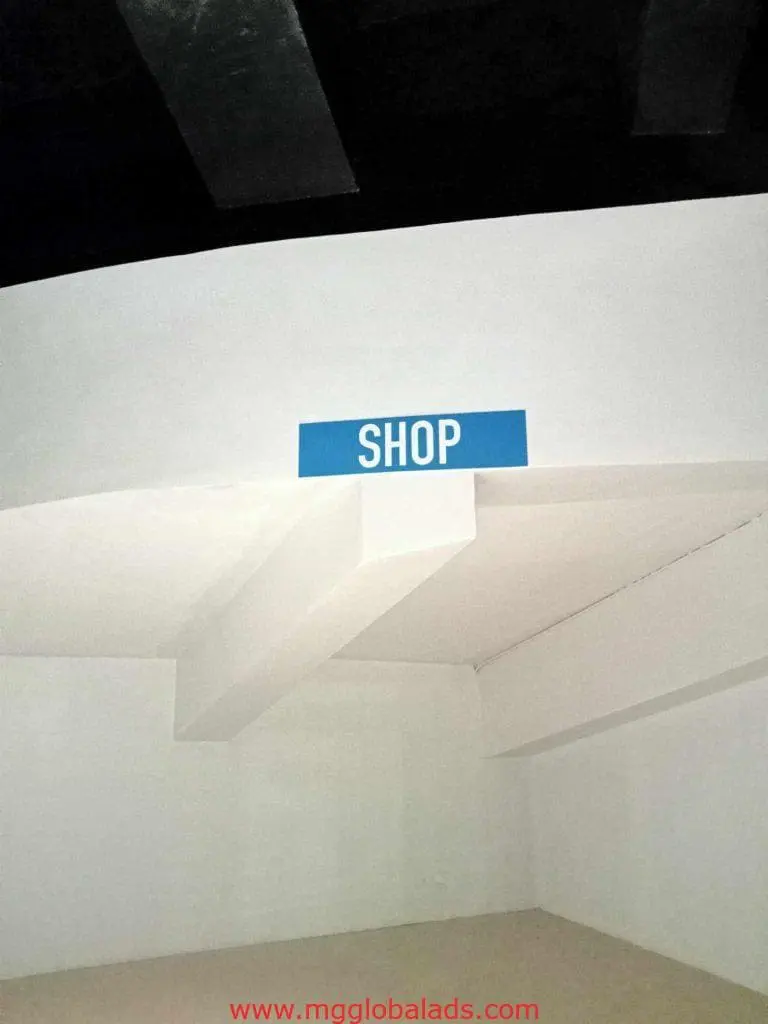 Blue metallic storefront sign with SHOP in white letters on a white wall in Makati, by M&G Global Ads.
