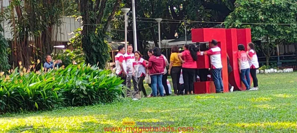 Outdoor 3D letter signage installation in Makati, with team in red and white shirts posing on grass, by M&G Global Ads.