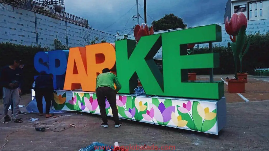 SPARKE LED signage install in Makati with flower base, three workers, outdoor among pots and buildings by M&G Global Ads.