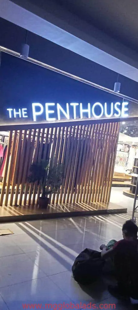 LED signage for THE PENTHOUSE above modern wooden entrance in BGC; person with bags nearby, by M&G Global Ads.