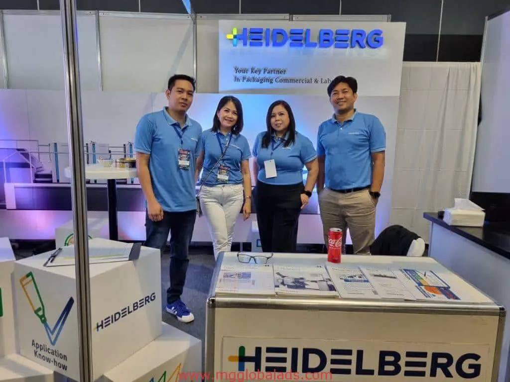 Four staff in blue shirts at a Heidelberg expo booth with metallic company signage in Makati by M&G Global Ads.