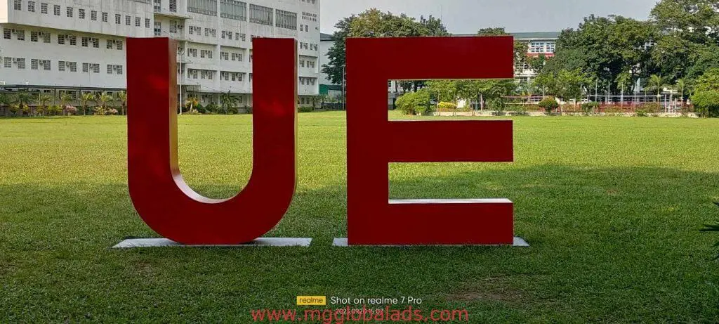 School building fabricated metal channel letters signage UE on a grassy field in Quezon City, trees and buildings behind, by M&G Global Ads.