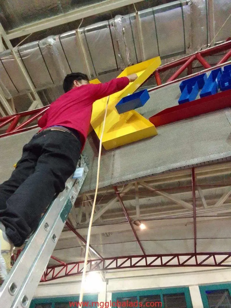 Building channel letter LED neon signage installation in Mandaluyong, technician mounting yellow E on metal frame by M&G Global Ads.
