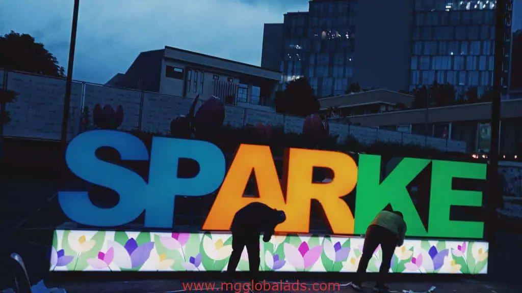 Custom metallic SPARKE signage with floral base, installed outdoors in Makati at dusk, by M&G Global Ads.