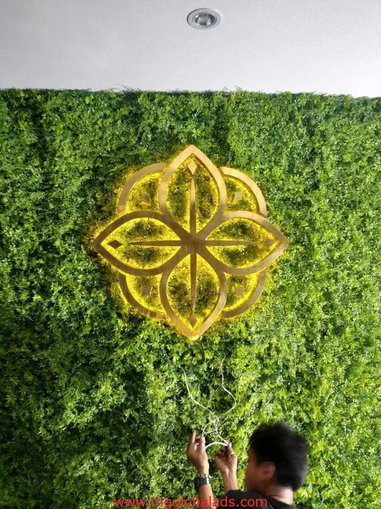 Acrylic flower logo signage on green plant wall, wiring adjusted by staff, in Makati installation by M&G Global Ads.