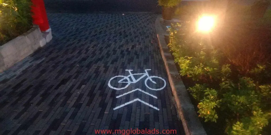 Illuminated bike lane directional signage on brick path beside green shrubs in Makati by M&G Global Ads.