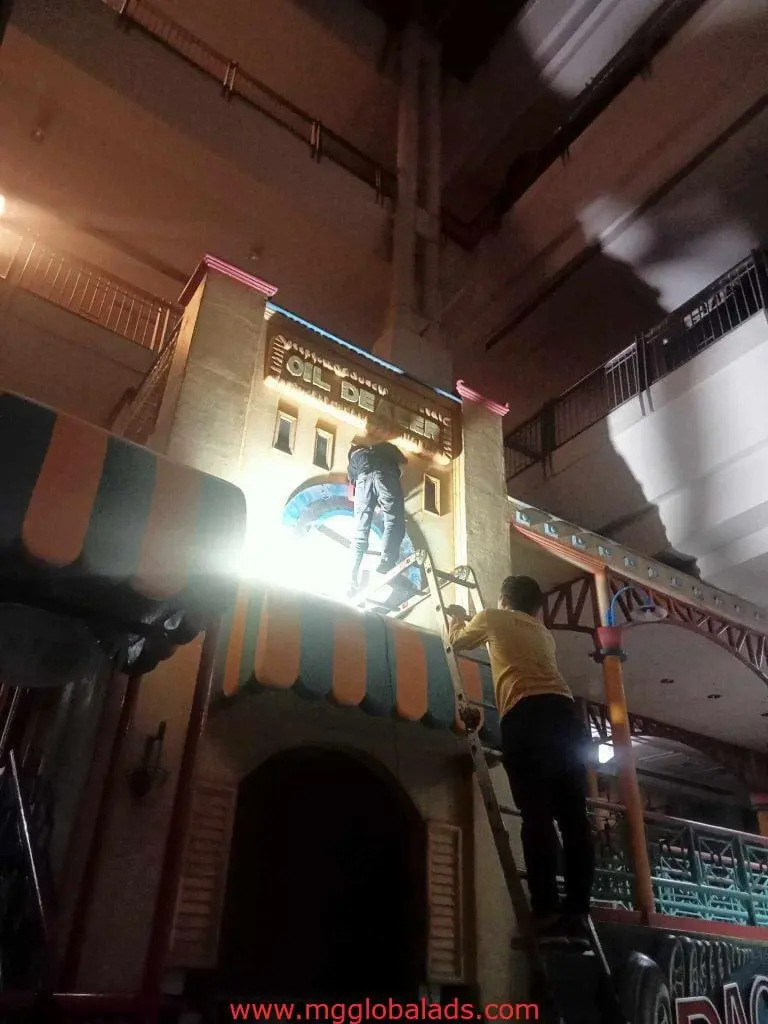 LED neon signage installation above an entrance at night in Makati, with workers on ladder and roof, by M&G Global Ads.