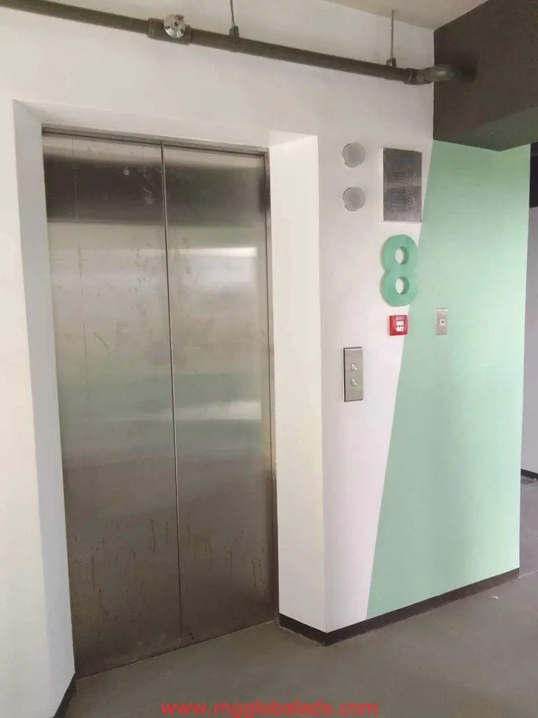 Metallic floor number signage on a stainless steel elevator door, white-mint wall, in Makati. By M&G Global Ads.