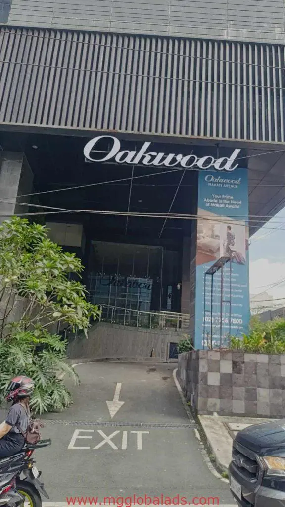 Oakwood LED signage and blue promo banner at a building entrance in Makati, exit driveway visible, by M&G Global Ads.