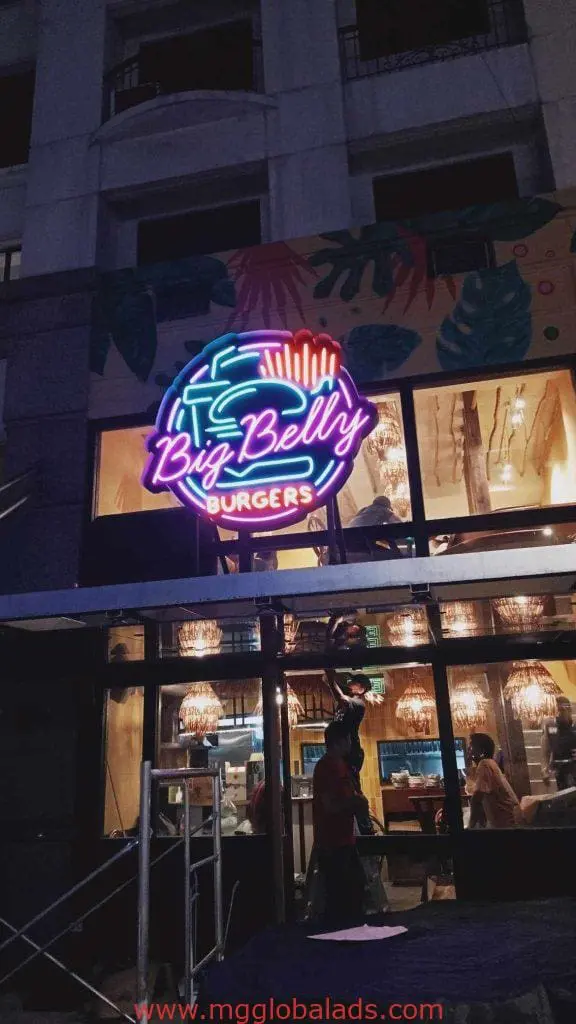 Big Belly Burgers metallic restaurant LED neon signage in Makati with glowing lights, cozy interior, and visible patrons by M&G Global Ads.