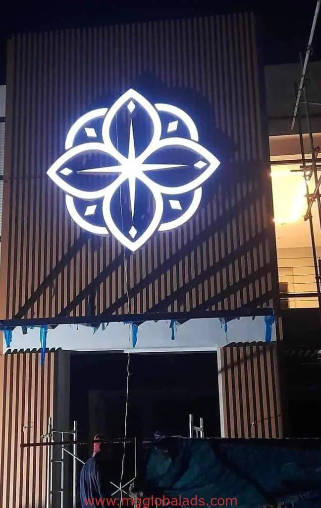 Illuminated acrylic geometric floral signage on building facade at night in Makati, with worker and scaffolding, by M&G Global Ads.