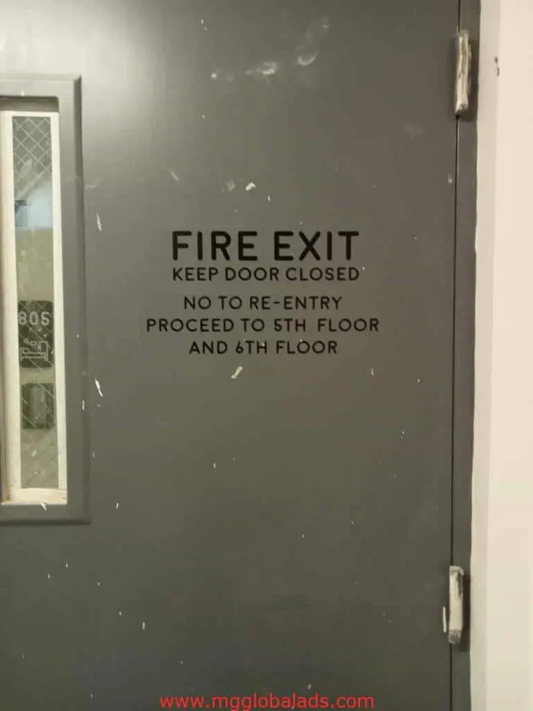 Fire exit metallic signage on gray door, small window left, in Makati building by M&G Global Ads.