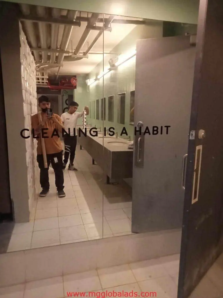 Acrylic signage CLEANING IS A HABIT in a bathroom mirror, two men reflected, selfie and mop. Makati. by M&G Global Ads.