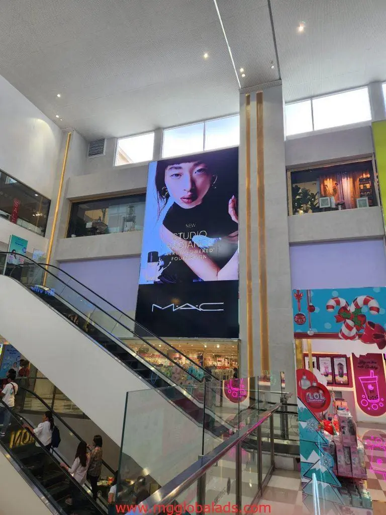 MAC Cosmetics LED signage above escalators in a vibrant Makati mall, colorful stores and shoppers visible, by M&G Global Ads.