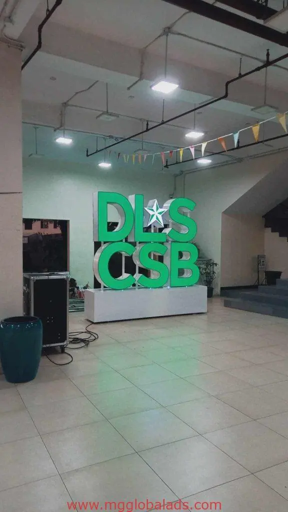 DLS CSB green acrylic indoor signage with star on white platform, colorful pennant banners, Makati location by M&G Global Ads.