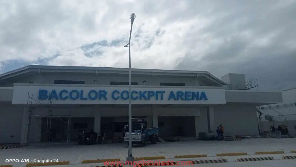 LED signage for Bacolor Cockpit Arena at a wide building, vehicles and workers in front, cloudy sky, Makati. By M&G Global Ads.