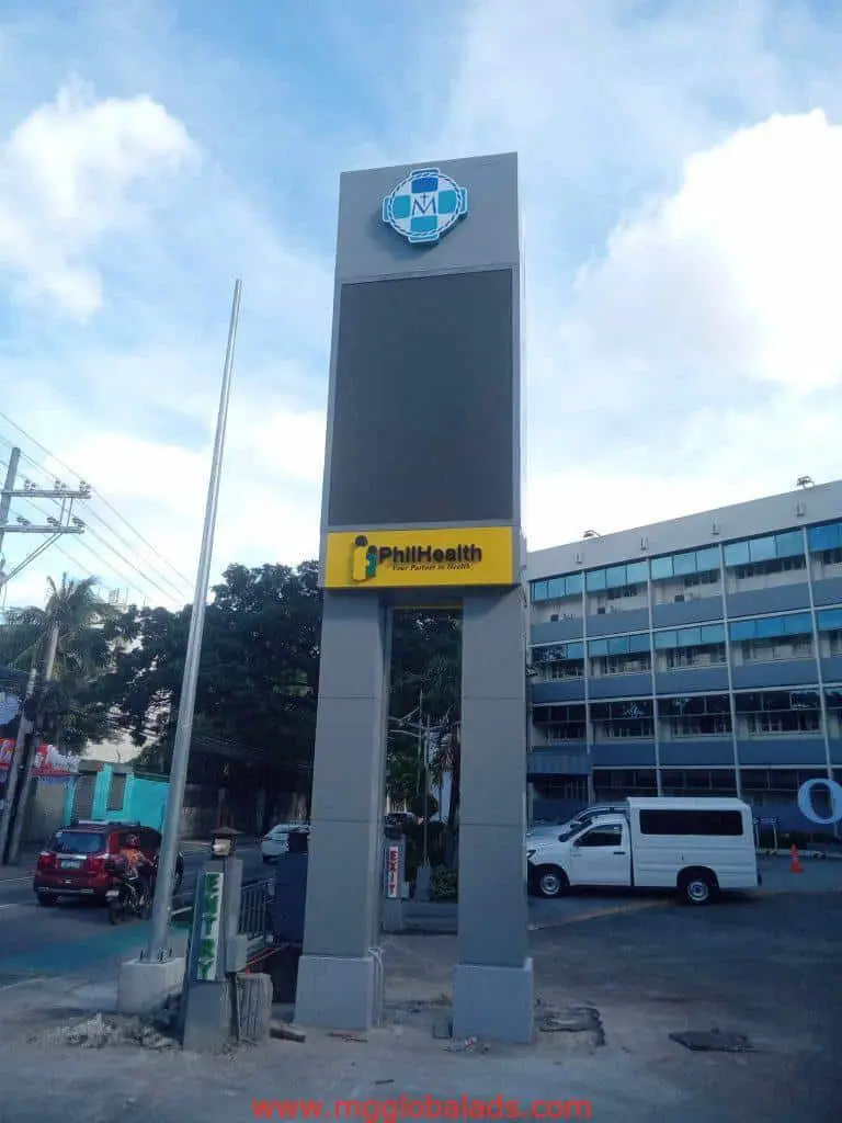 Outdoor pylon signage SM Mall and PhilHealth, parking lot in Makati, cars and buildings visible, by M&G Global Ads.