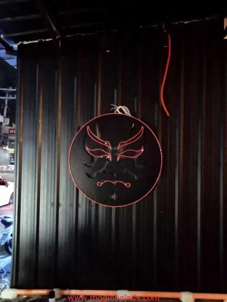 Neon LED mask signage on a dark ridged wall in Makati, red and white outline facial features, by M&G Global Ads.