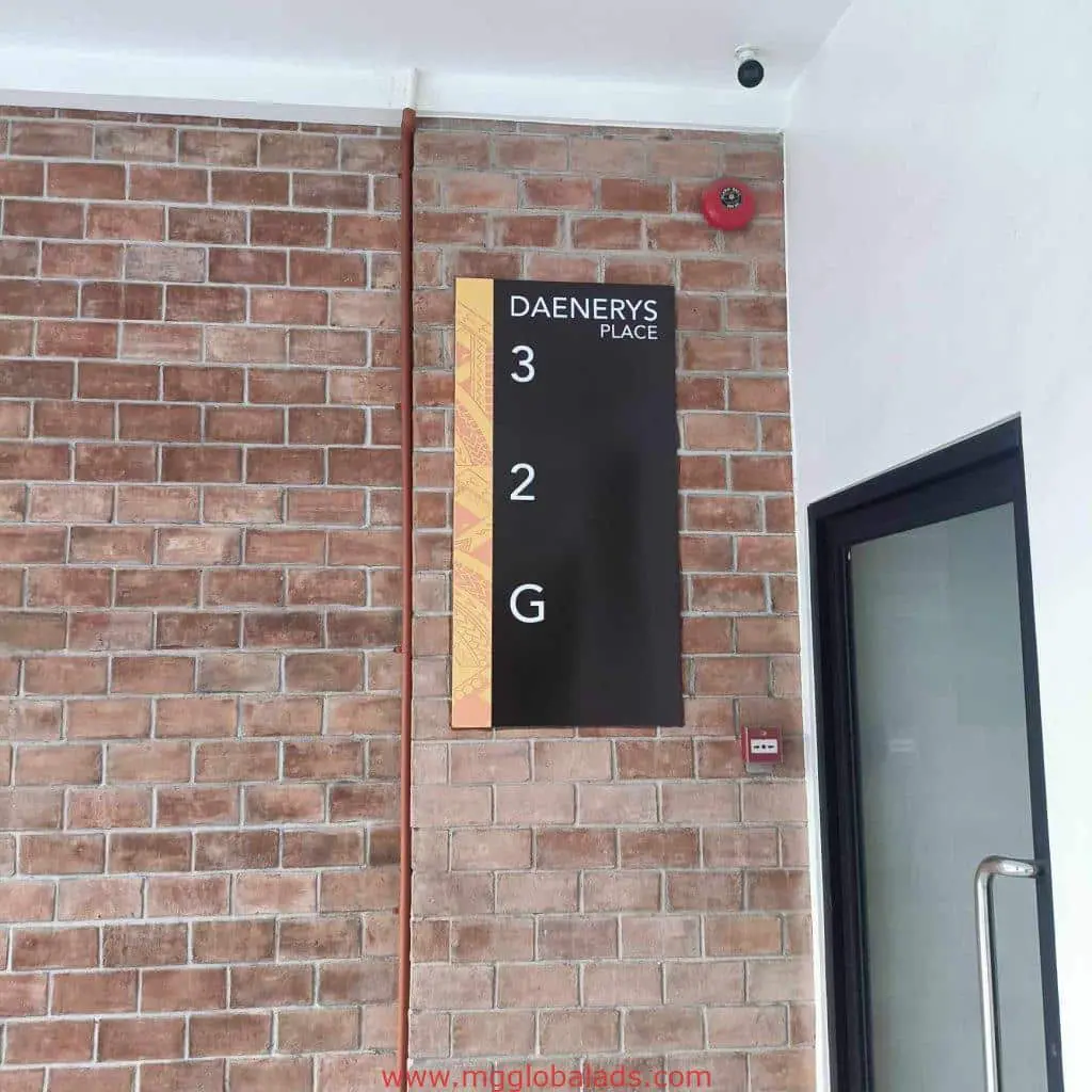 Building signage for DAENERYS PLACE on brick wall in Mandaluyong with floor list, glass door, and security camera by M&G Global Ads.