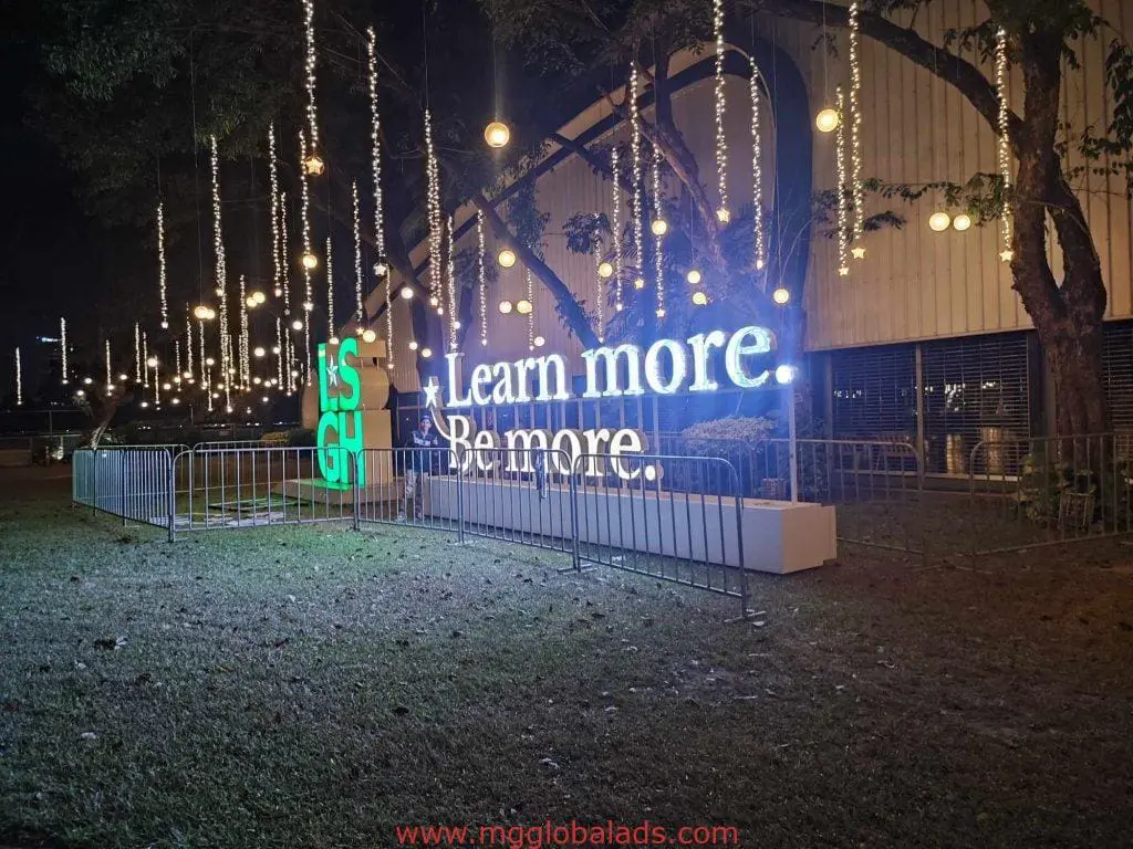 Metallic building signage for Learn more. Be more. in Quezon City, with string lights and barricade at night by M&G Global Ads.