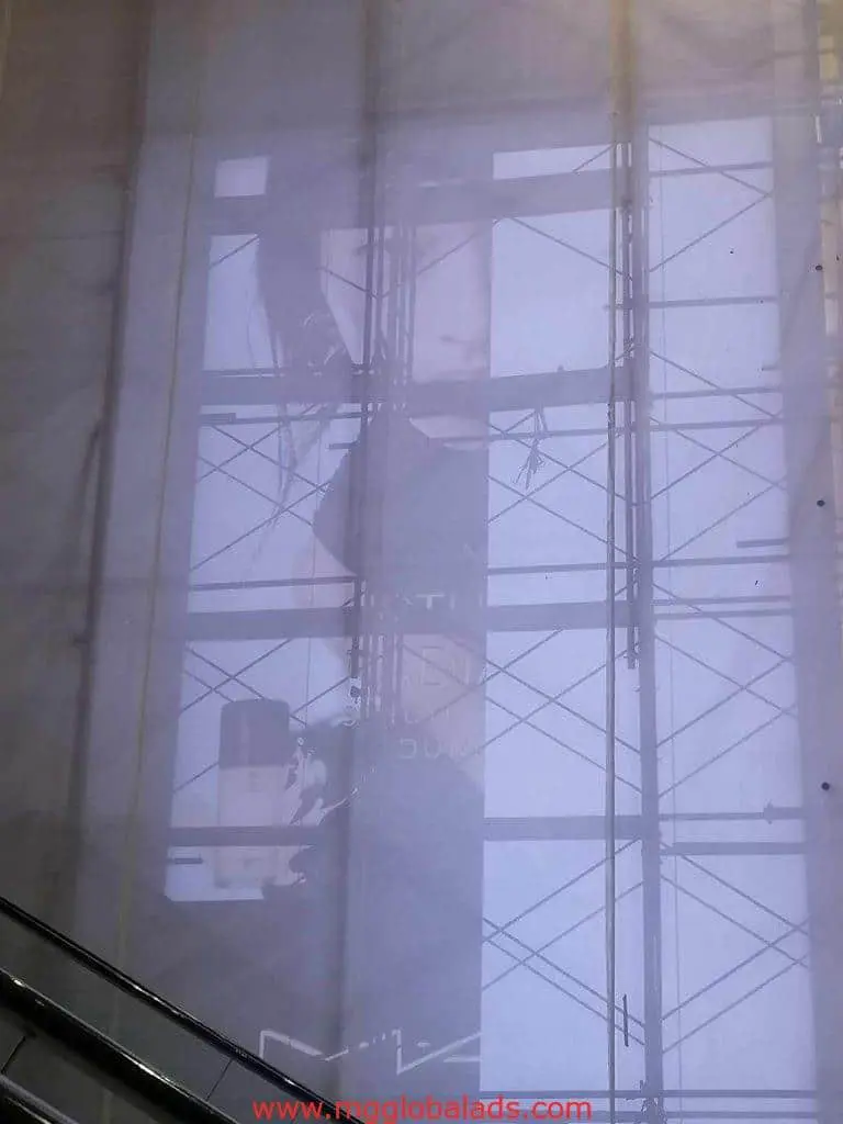 Billboard signage ad featuring a person and product, viewed through scaffolding in Makati, metal beams and escalator foreground, by M&G Global Ads.