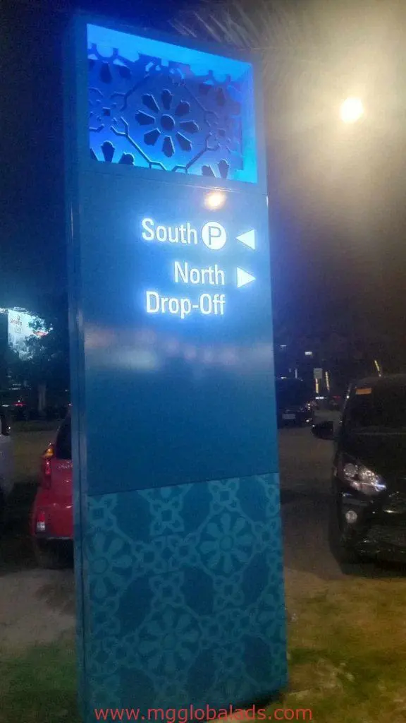 Directional wayfinding sign with arrows for South P and North Drop-Off in Makati at night, cars parked nearby by M&G Global Ads.