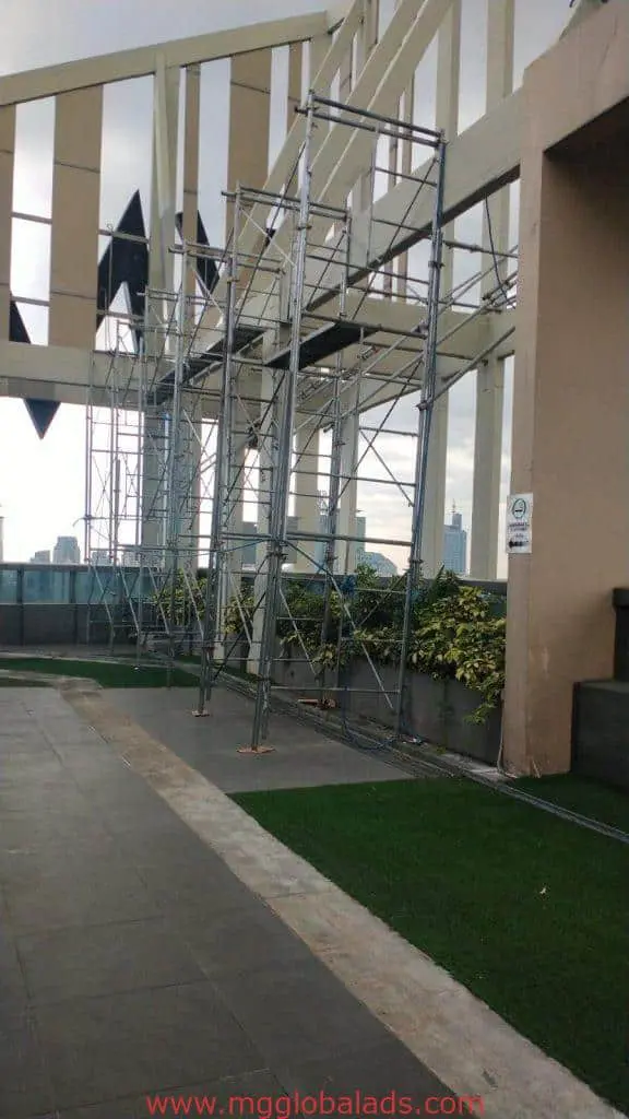 Billboard signage installation on rooftop with scaffolding in Makati, beige building, cityscape and plants—by M&G Global Ads.