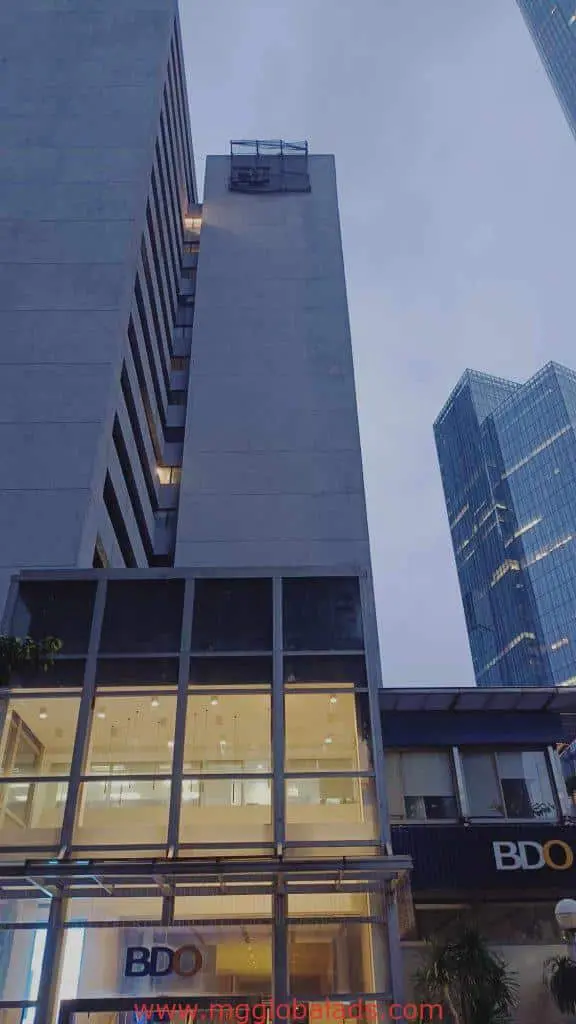 Metallic BDO building signage in Makati on modern glass towers at dusk with cloudy sky, by M&G Global Ads.