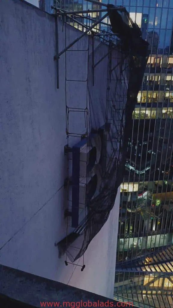Acrylic letter B building signage in Makati, partly covered by scaffolding and netting at dusk, by M&G Global Ads.
