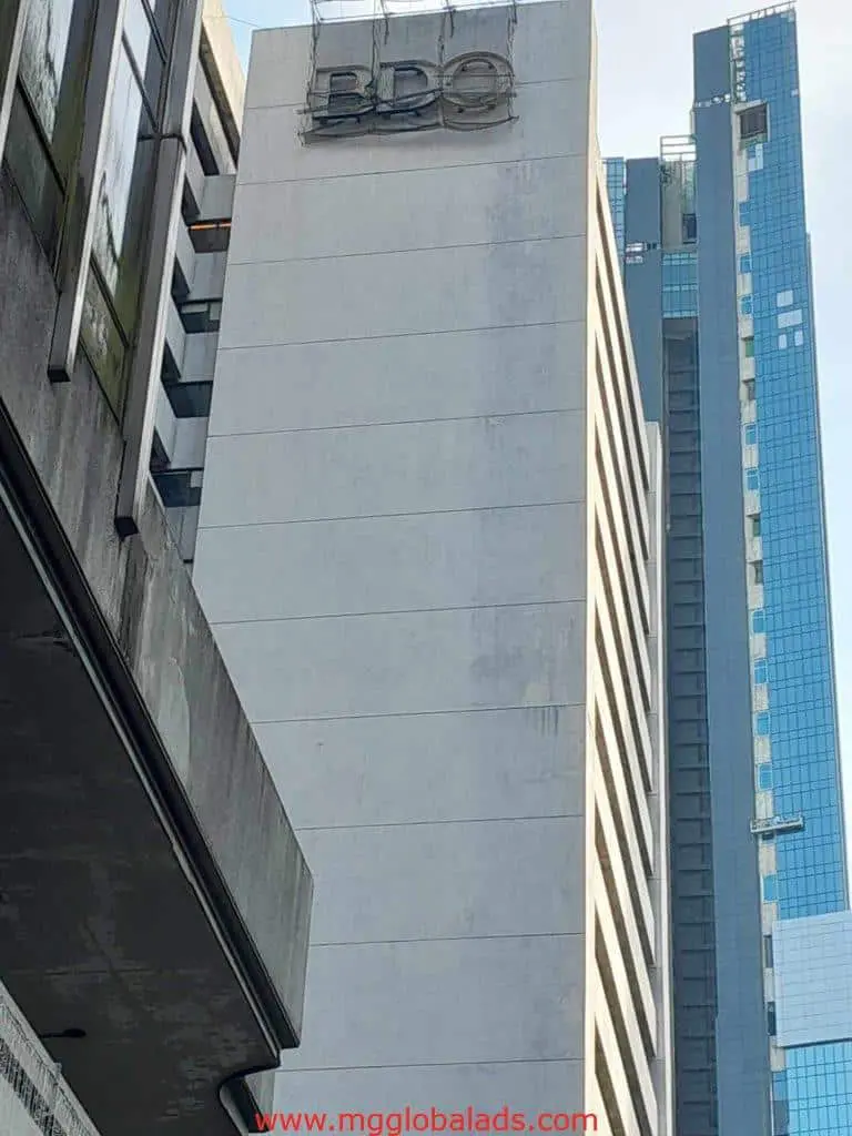 Metallic BDO rooftop signage on a tall white building in Makati, surrounded by modern high-rises. By M&G Global Ads.