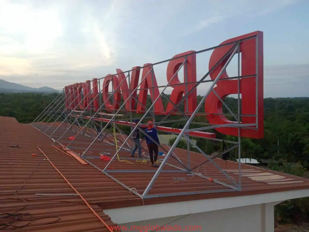 Workers installing red metal rooftop signage with frame in Mandaluyong—outdoor sign installation by M&G Global Ads.