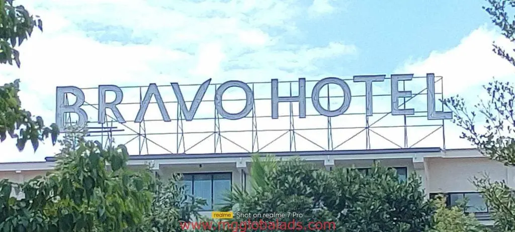 Metallic hotel signage for Bravo Hotel above building with trees in Quezon City, cloudy sky, by M&G Global Ads.