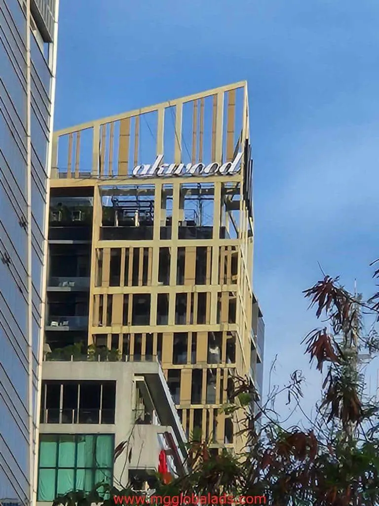 Modern building with gold beams and acrylic signage in Makati, blue sky and trees in background, by M&G Global Ads.