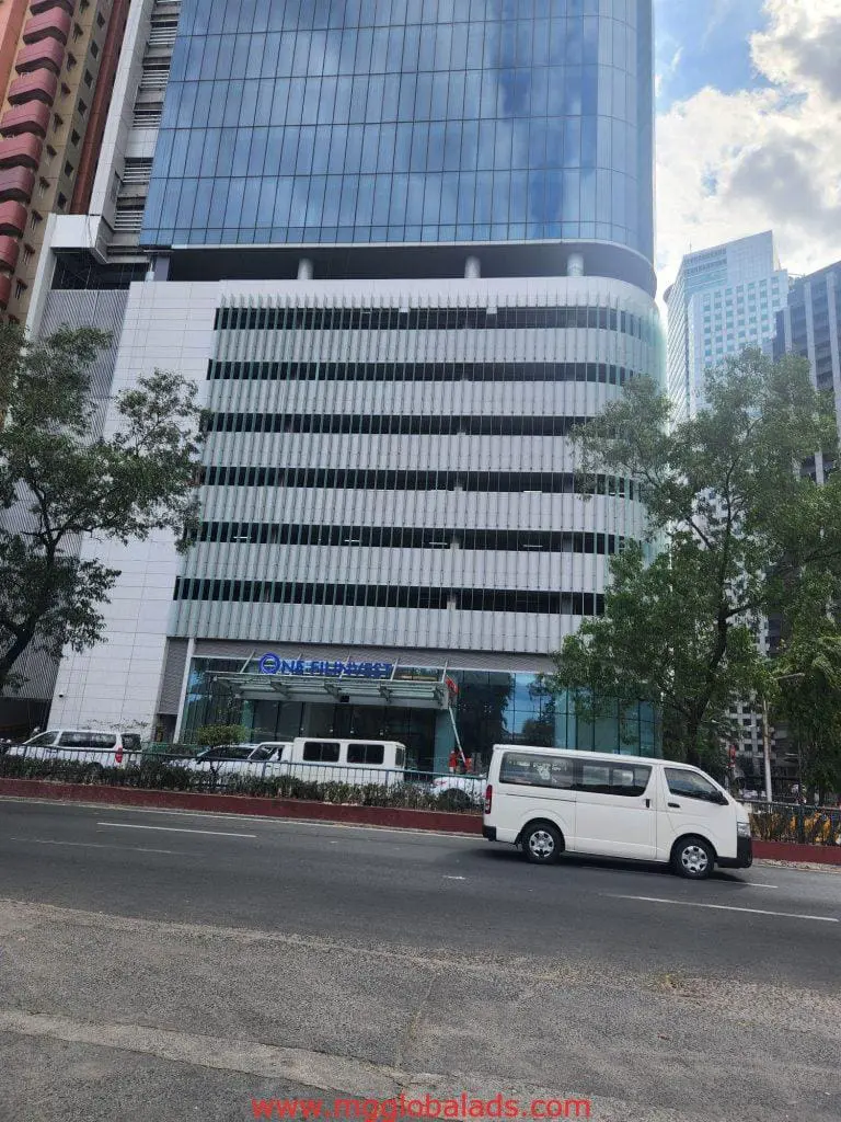 LED building signage on a modern office in Makati with glass panels, white van passing by, by M&G Global Ads.