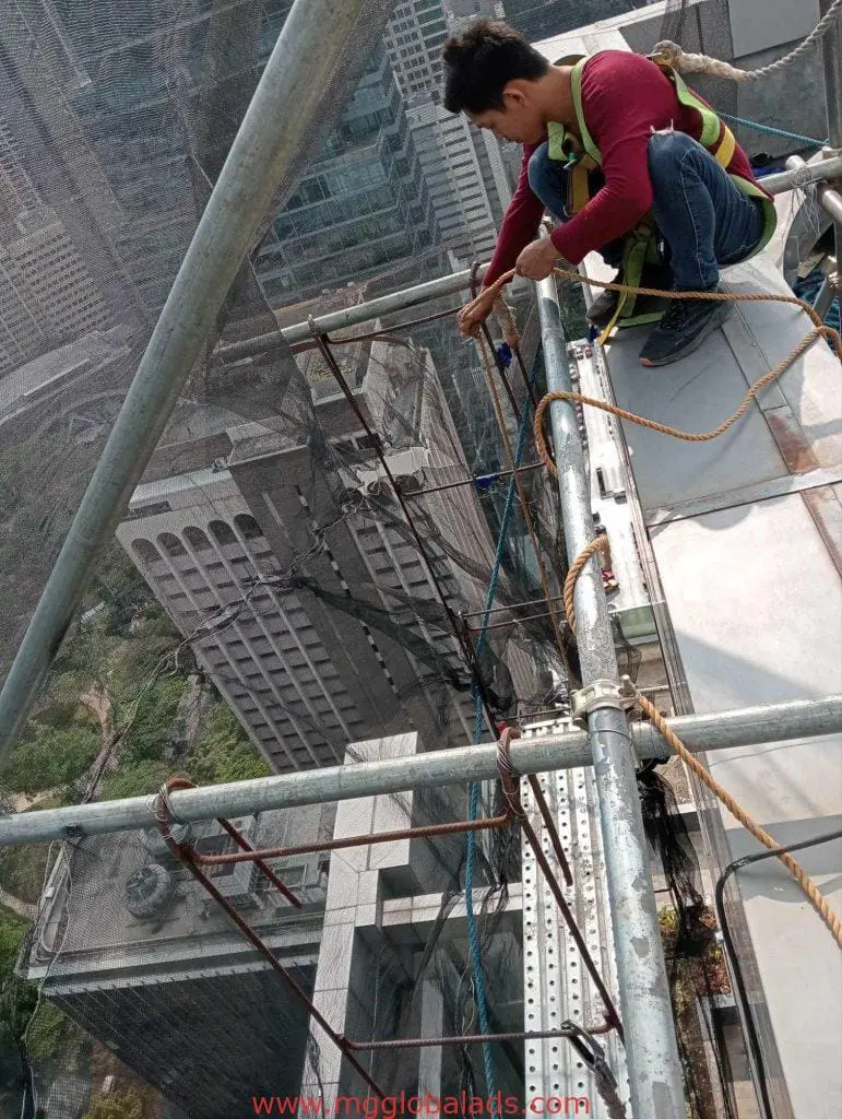 Billboard signage installation for commercial client in Makati, with worker on scaffolding above tall buildings, by M&G Global Ads.