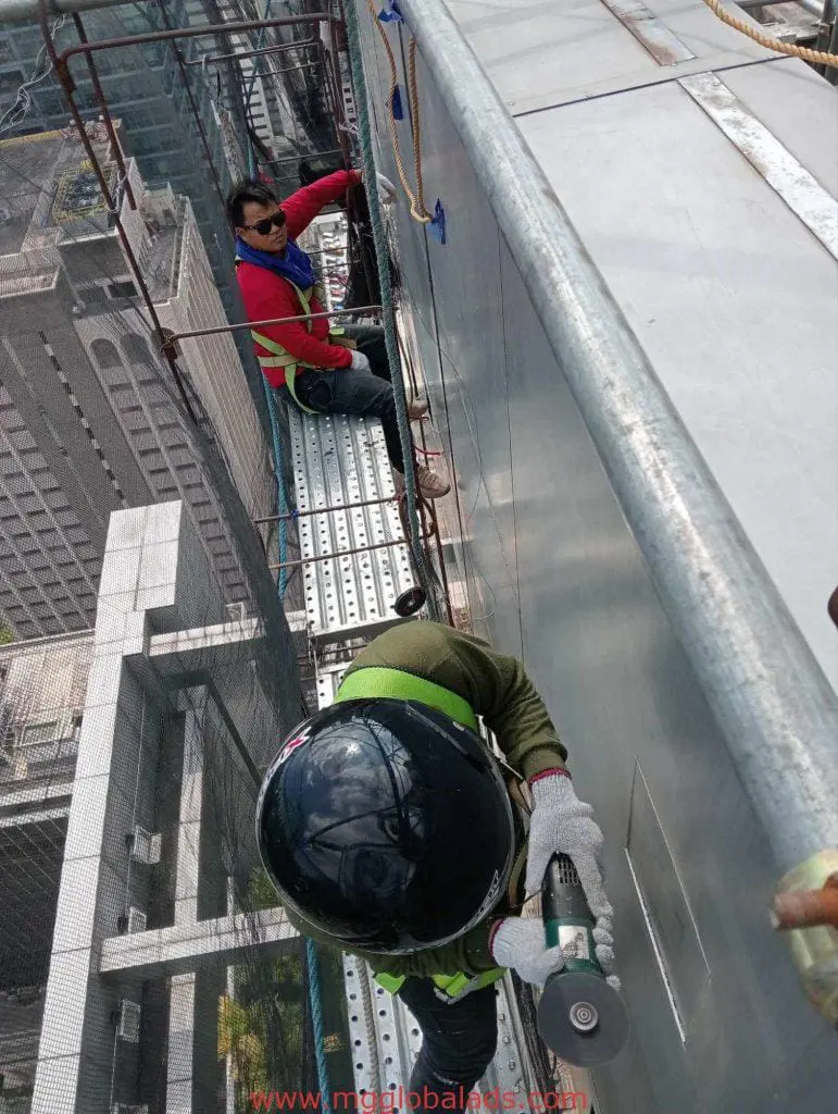 Workers installing a pylon sign for a client on scaffolding above Makati, with skyscrapers below, by M&G Global Ads.