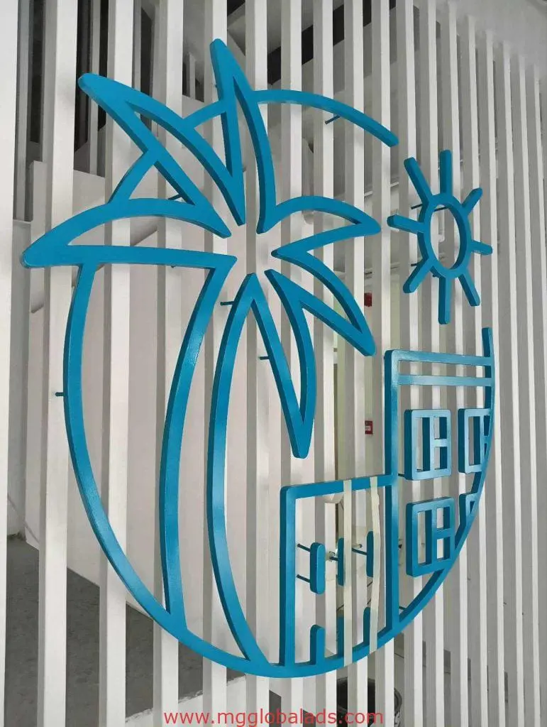 Blue metallic custom signage of stylized palm tree, sun, and building on white slats in Makati by M&G Global Ads.