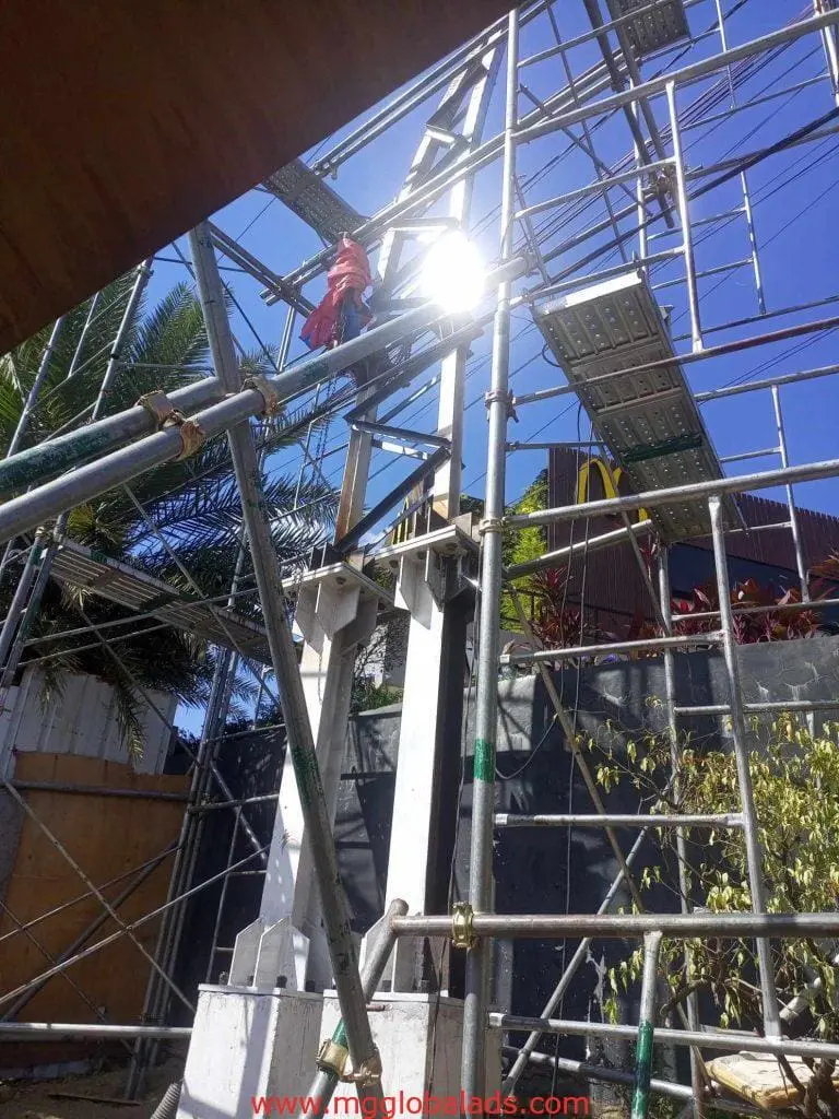 McDonalds pylon signage installation at a construction site in Makati with scaffolding, beams, and green plants by M&G Global Ads.