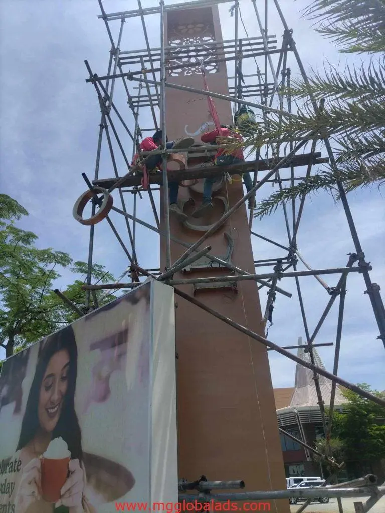 Acrylic outdoor signage billboard with palm trees and smiling woman in Makati; clock tower work scene by M&G Global Ads.