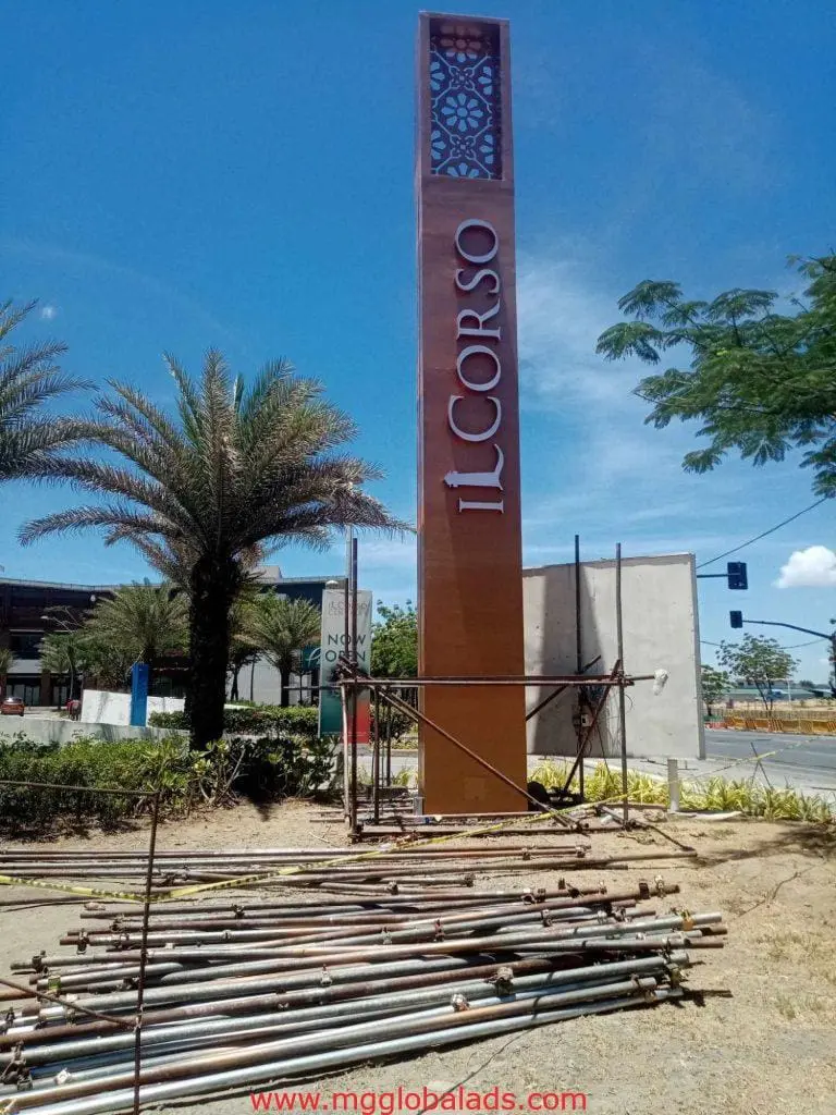Vertical IL CORSO outdoor signage in Makati beside a road with palm trees and construction materials by M&G Global Ads.